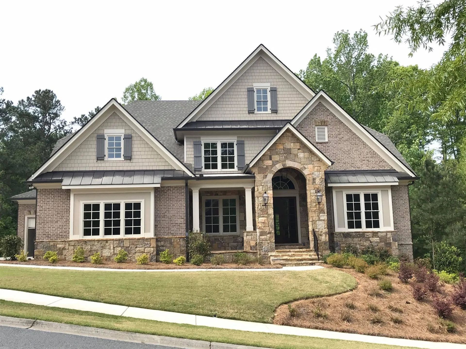 Two-story house with stone and brick exterior, brown roof, and manicured lawn.