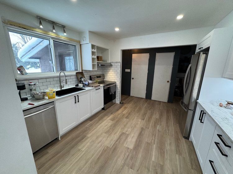 A kitchen with white cabinets , stainless steel appliances , hardwood floors and a large window.