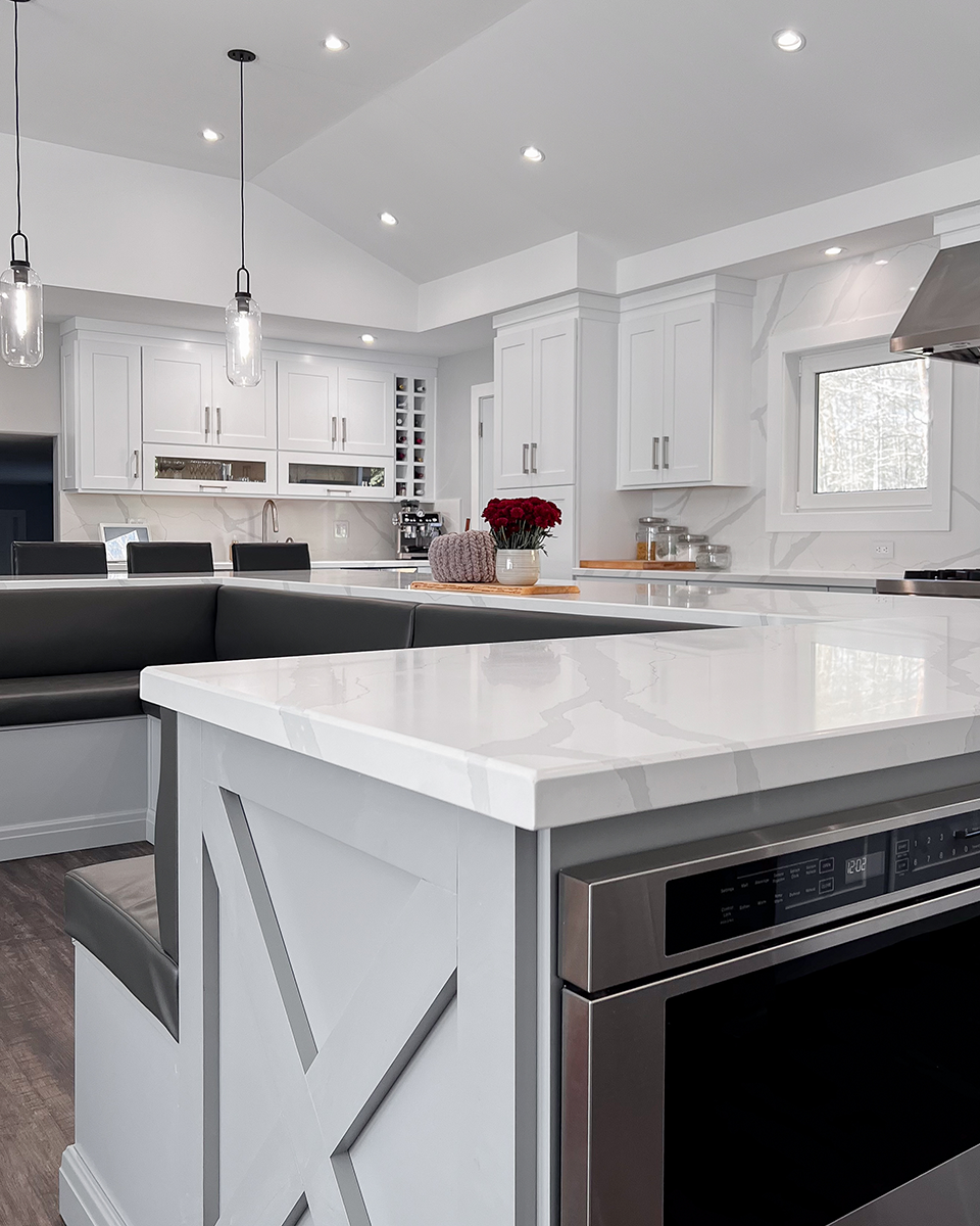 Modern white kitchen with island, gray accents, and built-in oven. Overhead lighting illuminates the space.