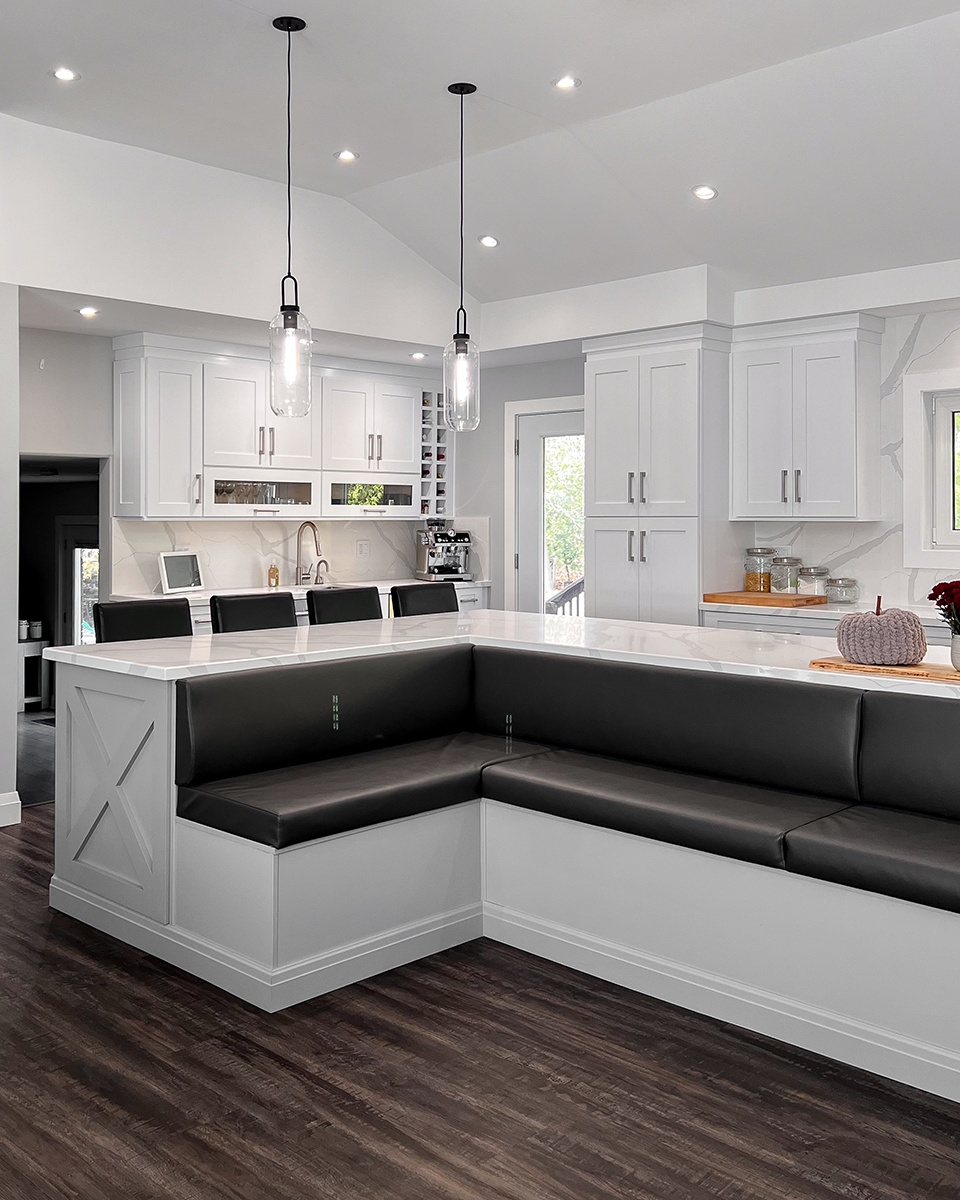Modern kitchen with a white island and built-in black leather bench seating. Two pendant lights hang above. Dark wood floors.