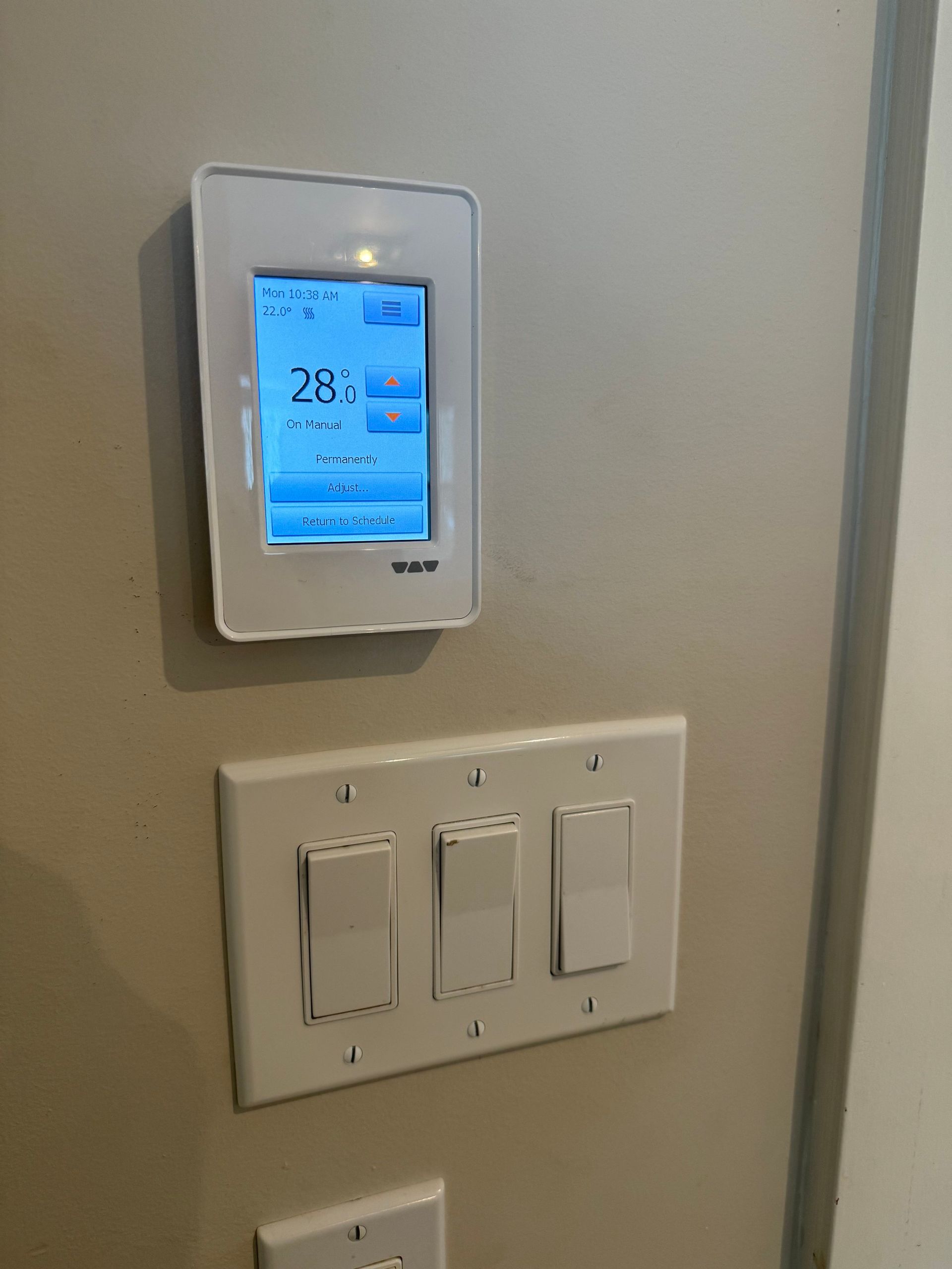 A thermostat is mounted on a wall next to three light switches.