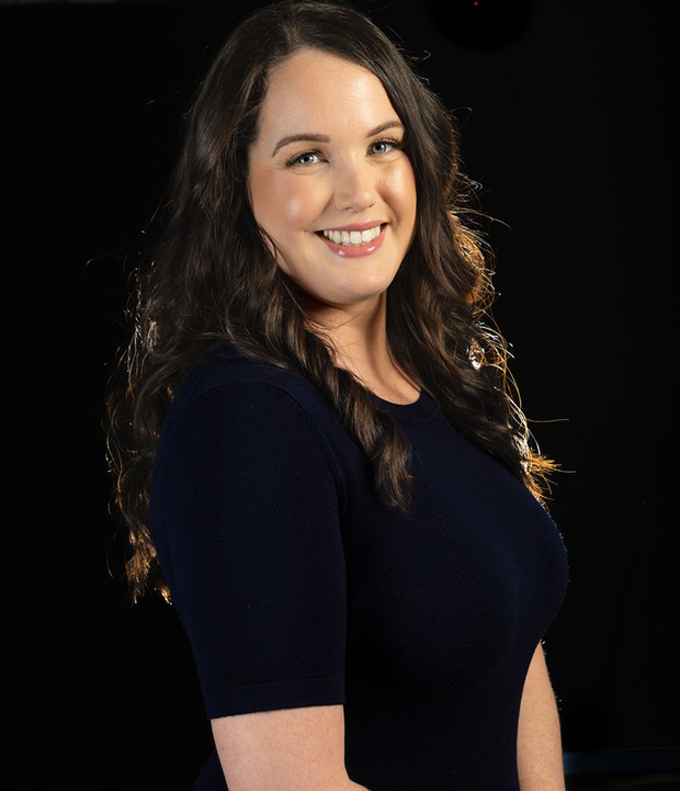 A woman in a blue dress is smiling in front of a black background