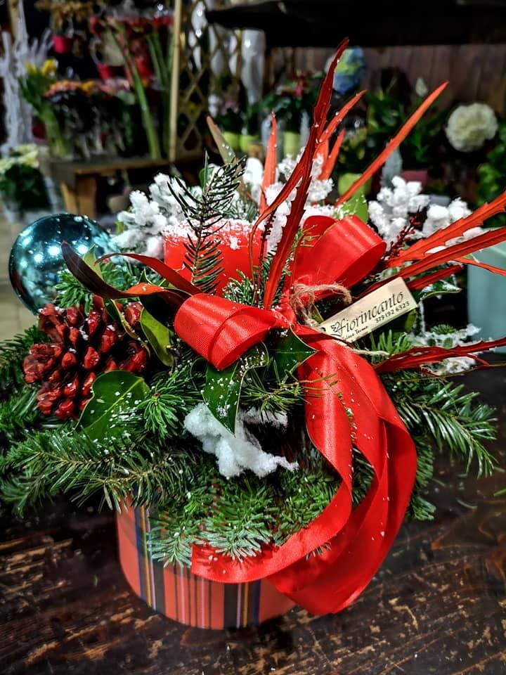 Una festosa composizione floreale natalizia in un vaso a righe con rami di pino, nastri rossi, ornamenti e dettagli innevati.