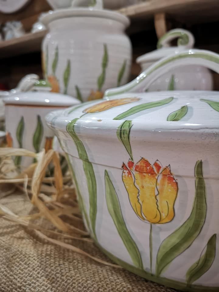 Barattoli da cucina in ceramica bianca dipinti a mano con motivi di tulipani gialli e foglie verdi, poggiati su una superficie di tela di iuta.