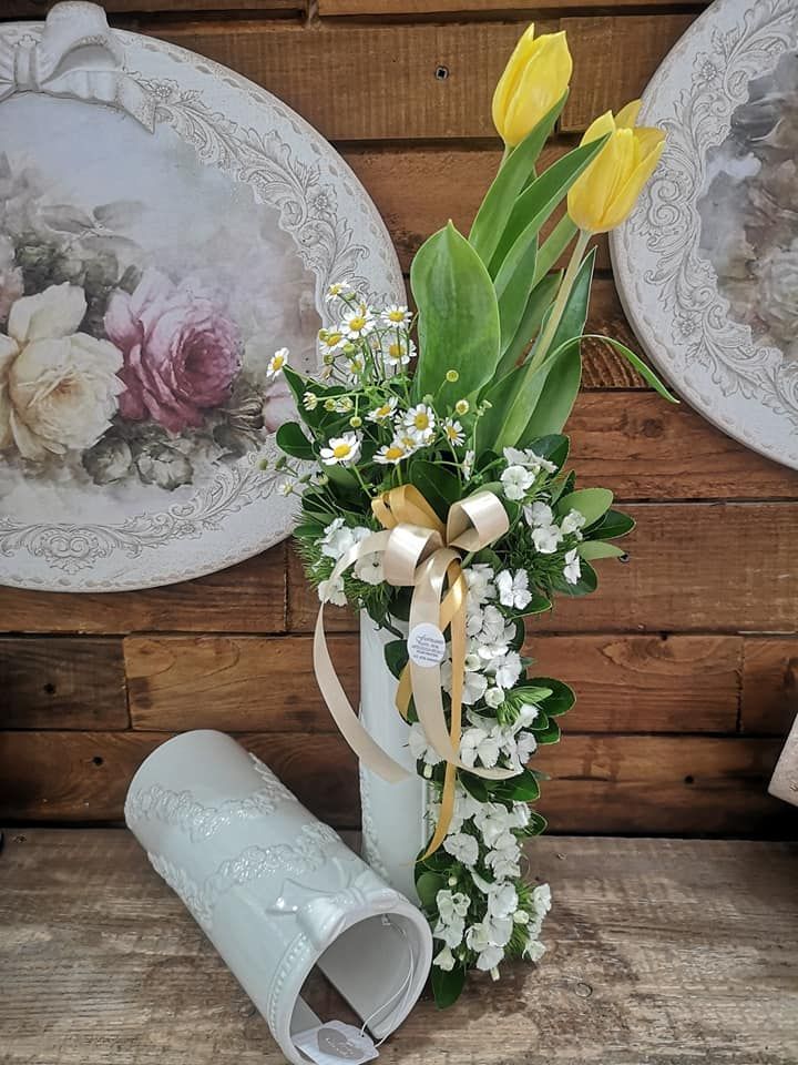 Due tulipani gialli e piccoli fiori bianchi disposti in un vaso bianco alto, con un vaso identico accanto.