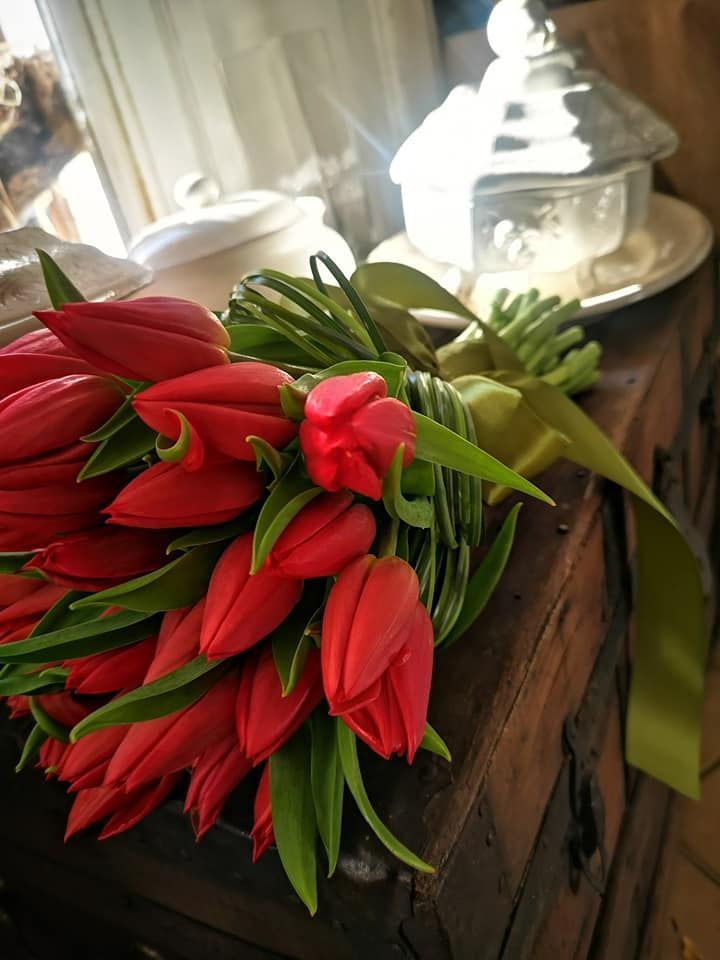 Un vivace bouquet di tulipani rossi con steli verdi, legato con un nastro coordinato, poggia su una rustica cassapanca di legno.