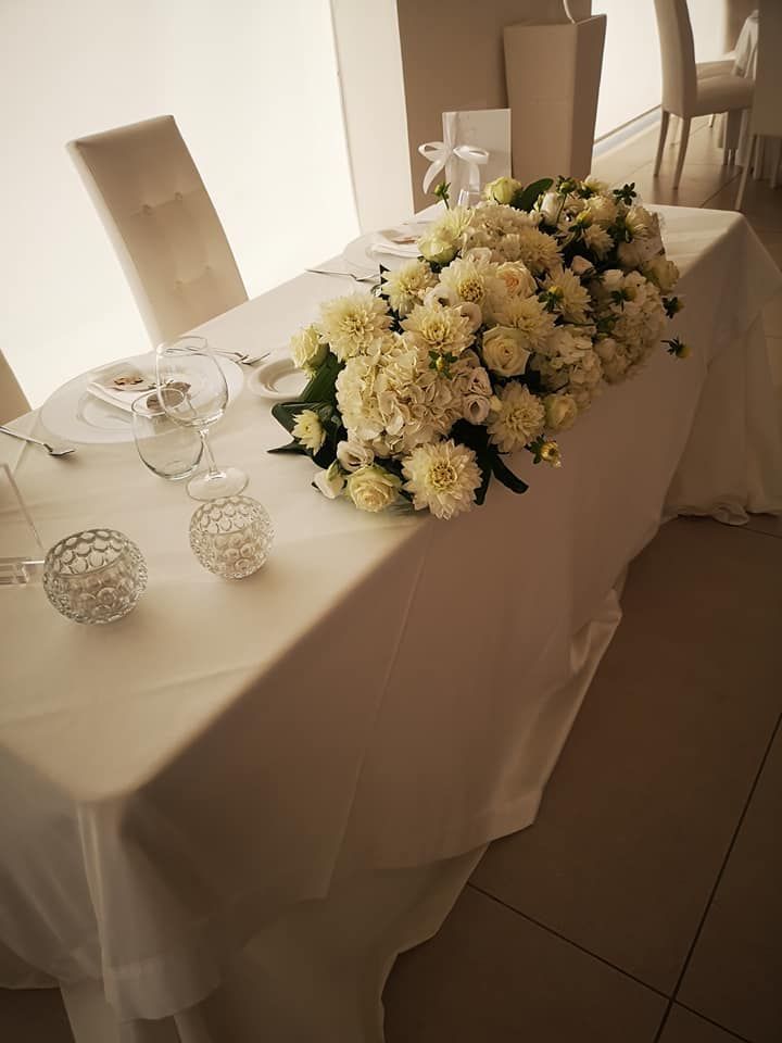 Un tavolo per gli sposi con una tovaglia bianca, portacandele di cristallo e un grande centrotavola di fiori bianchi.