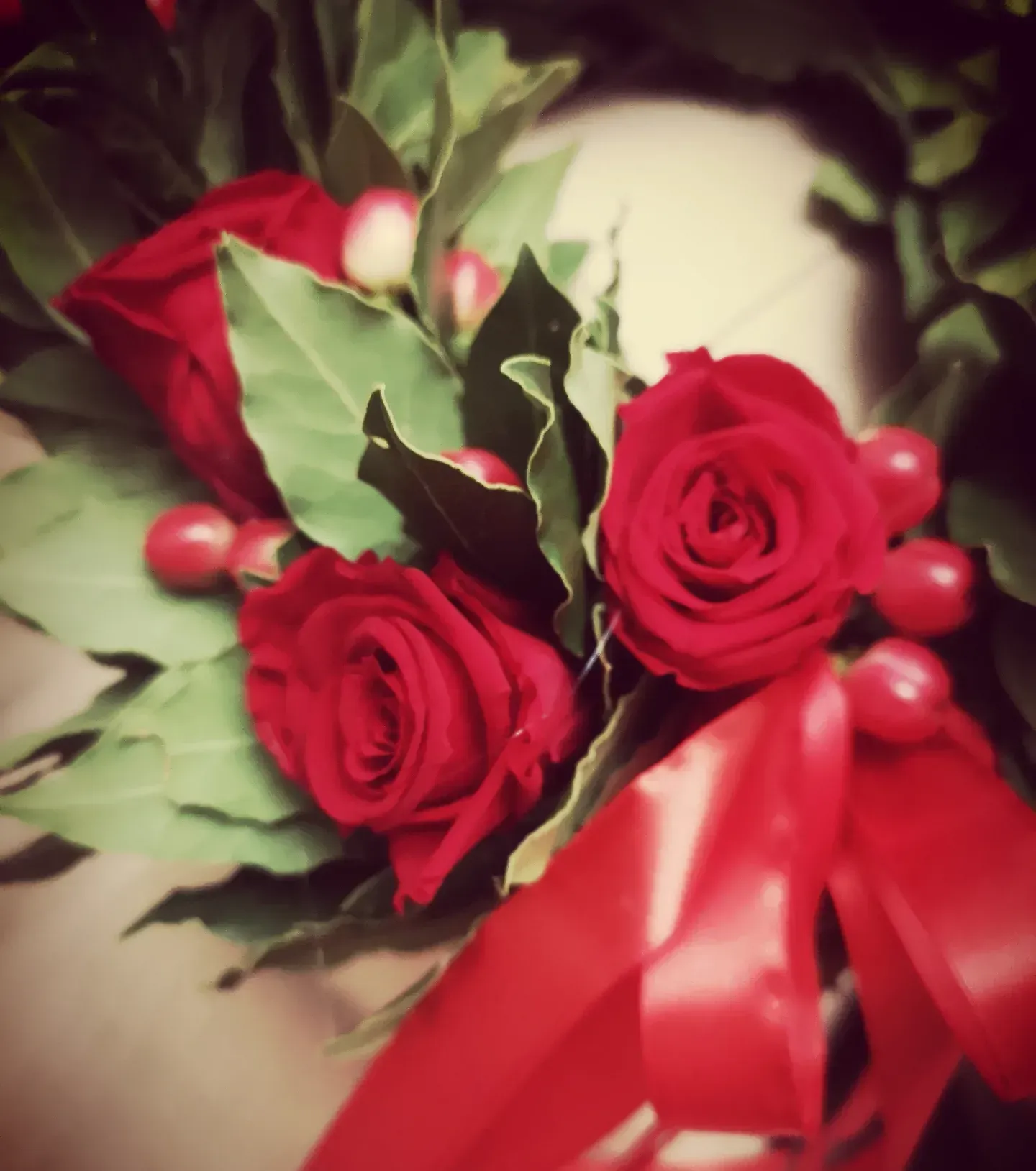 Una corona d'alloro ornata di rose rosse, piccole bacche rosse e un nastro rosso acceso.