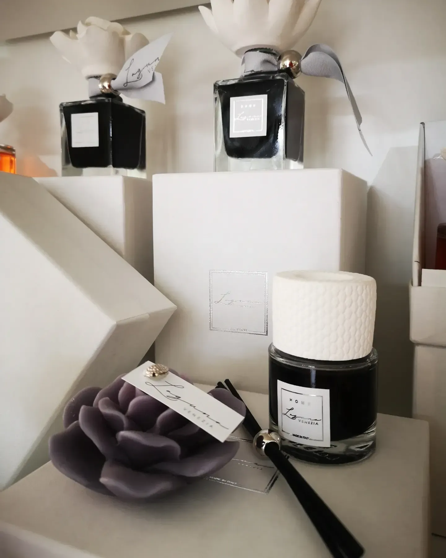 Una collezione di quattro diffusori a bastoncini con liquido scuro, decorati con fiori e con etichette del marchio, disposti su scatole bianche.