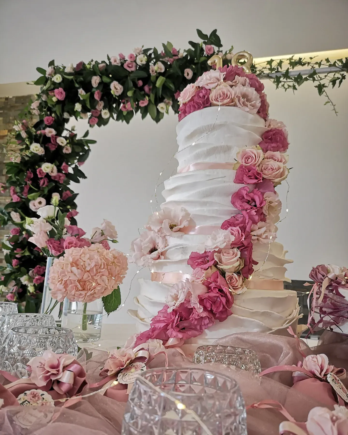 Una torta nuziale a più piani con glassa bianca dalla consistenza particolare, decorata con una cascata di rose rosa e bianche.