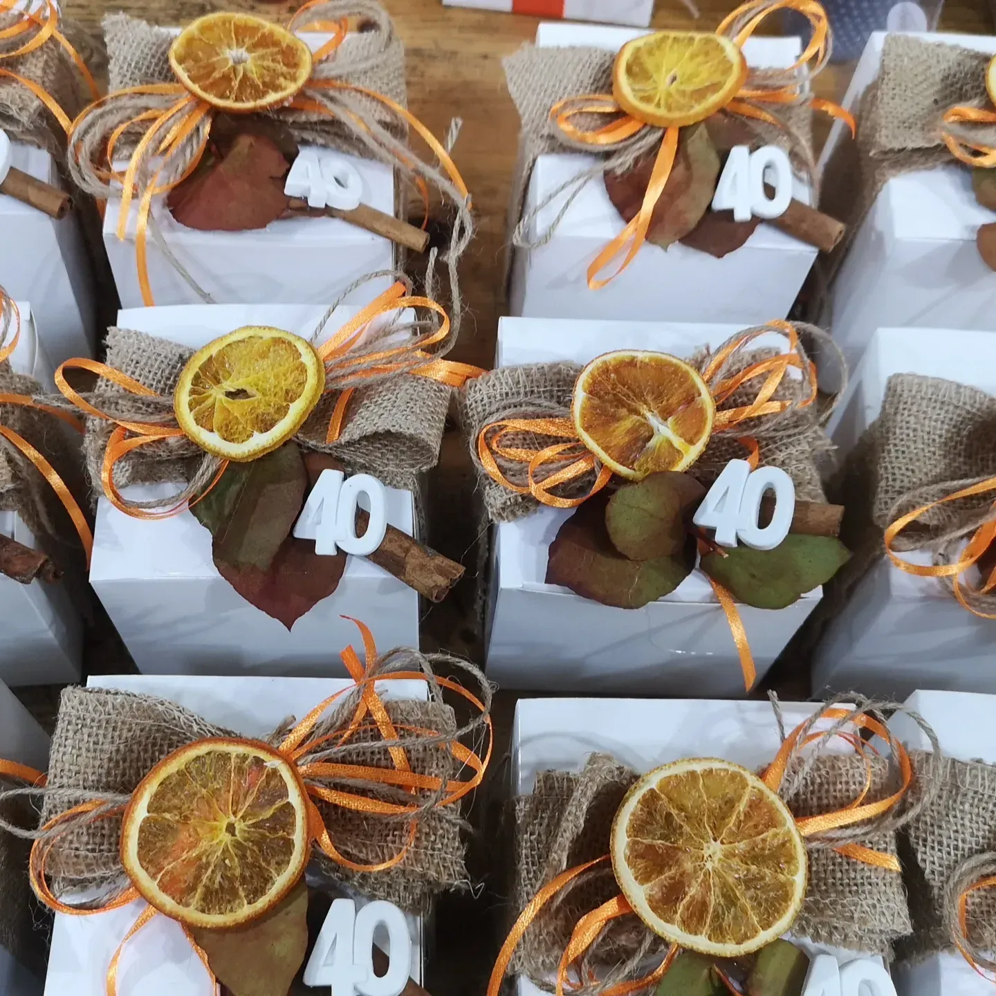 Scatoline bianche per bomboniere decorate con tela di iuta, spago, una fetta d'arancia essiccata, una foglia verde, un bastoncino di cannella e un'etichetta con il numero 