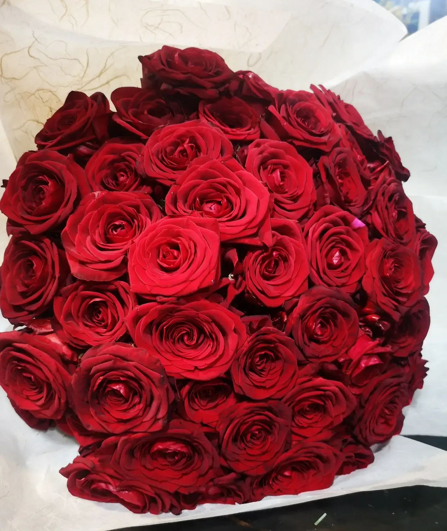 Un grande bouquet compatto di rose rosse brillanti, avvolto in carta velina bianca.