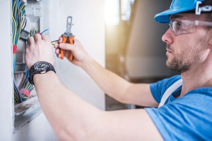 Electrician in blue hard hat wiring an electrical panel with pliers indoors