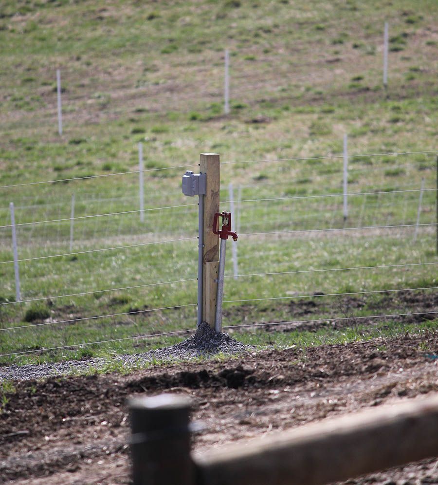 A wooden post with a red faucet attached to it in a field.