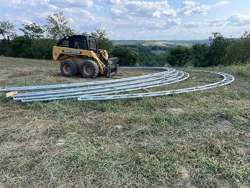 A bulldozer is moving a bunch of metal pipes in a field.