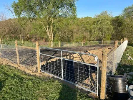 A black dog is behind a fence in a field.