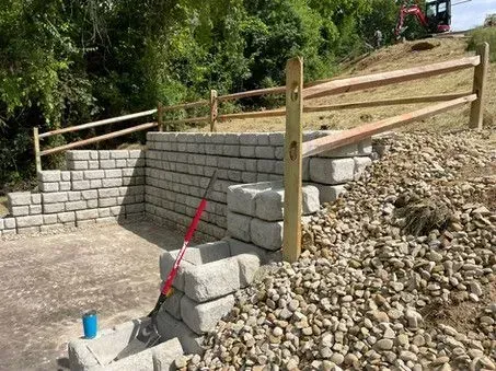 A brick wall is being built next to a pile of gravel and a wooden fence.