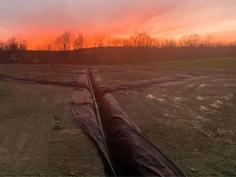 A sunset over a field with a fence in the foreground and trees in the background.