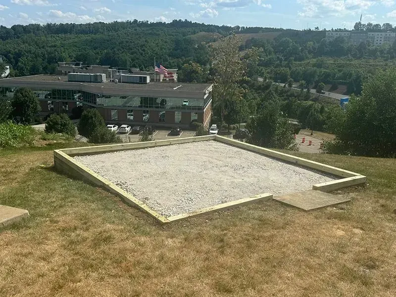 A sandbox is sitting on top of a grassy hill with a building in the background.