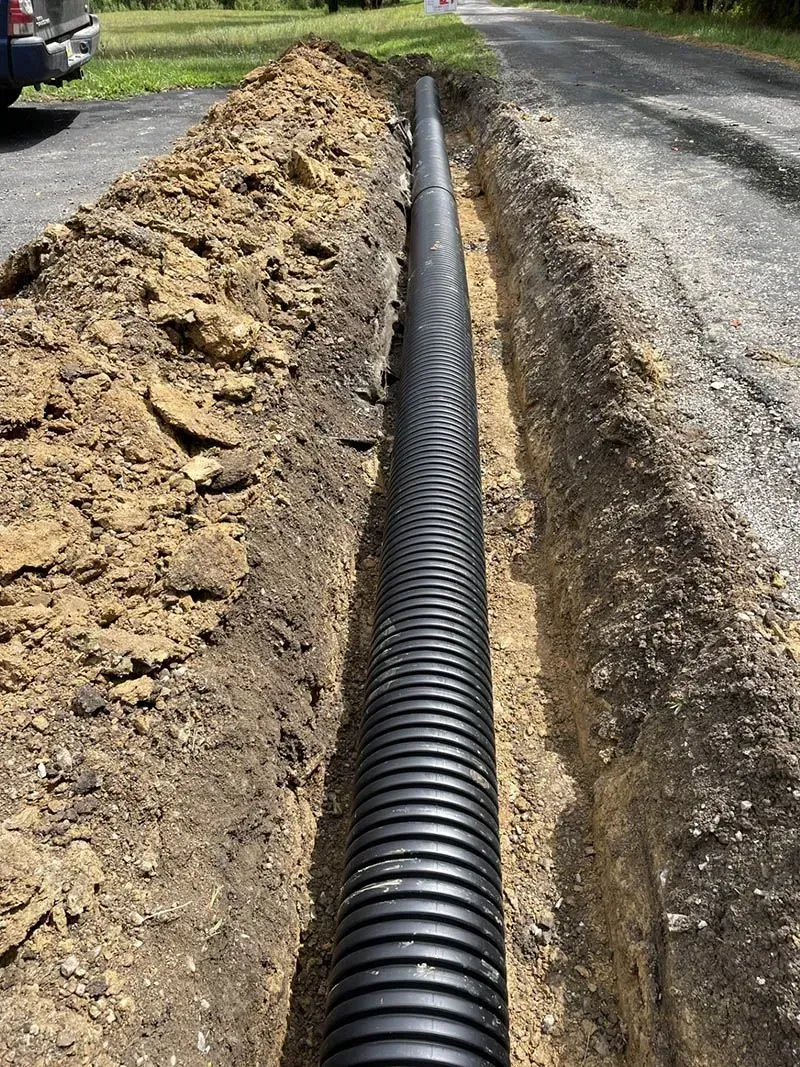 A black pipe is being installed in a trench next to a road.