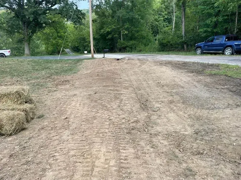 A blue truck is parked on the side of a dirt road.