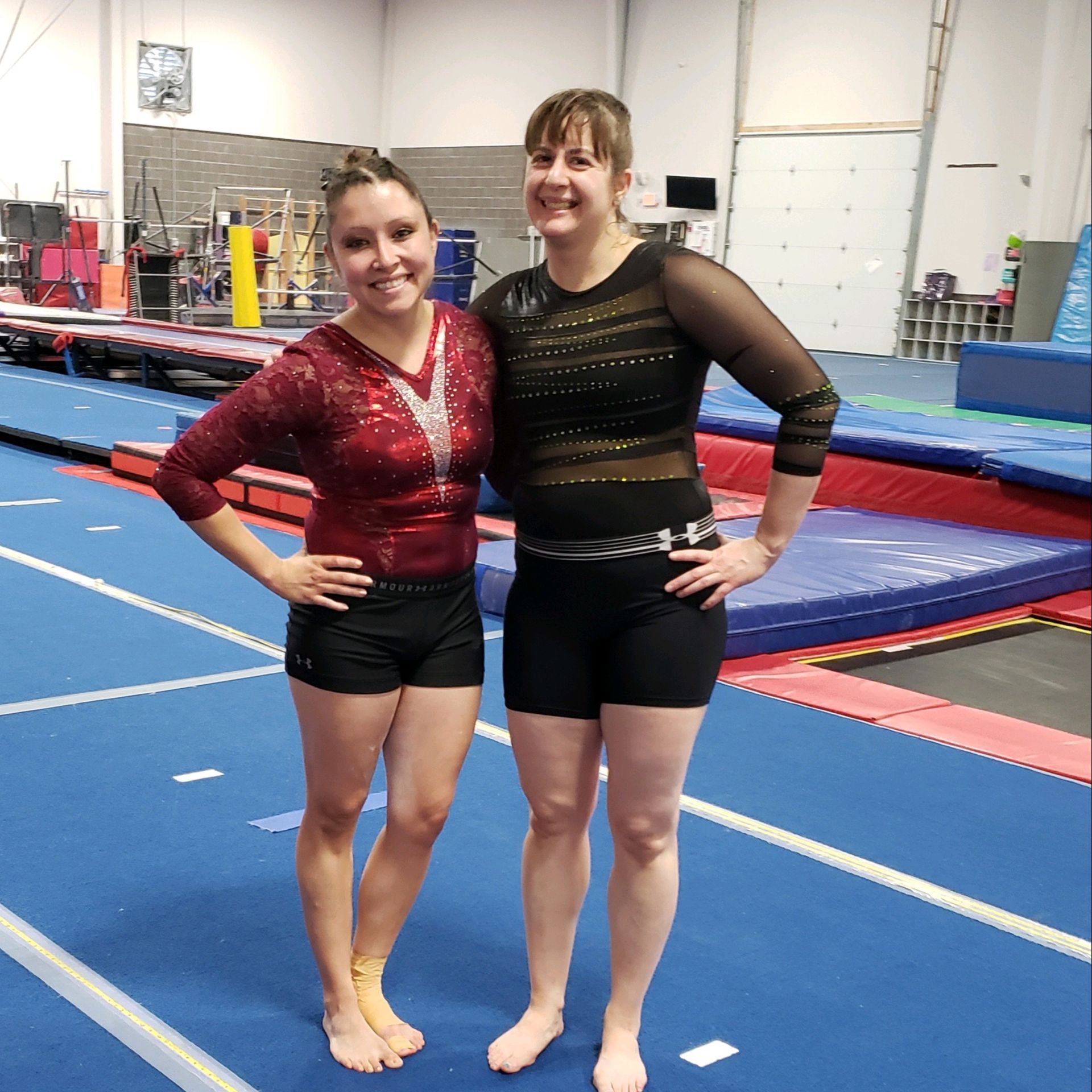 Two adult female gymnasts are posing for a picture in a gym