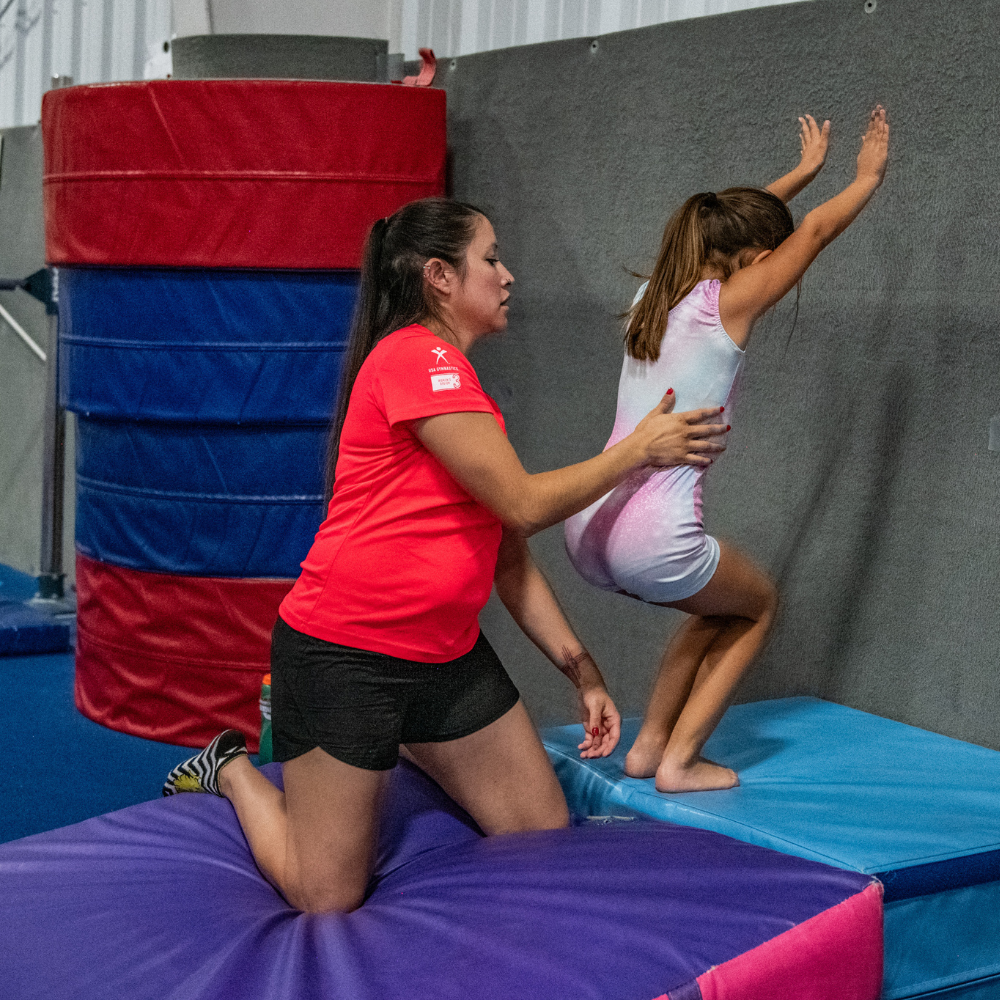 A coach is helping a little girl do a back handspring on a wedge mate.