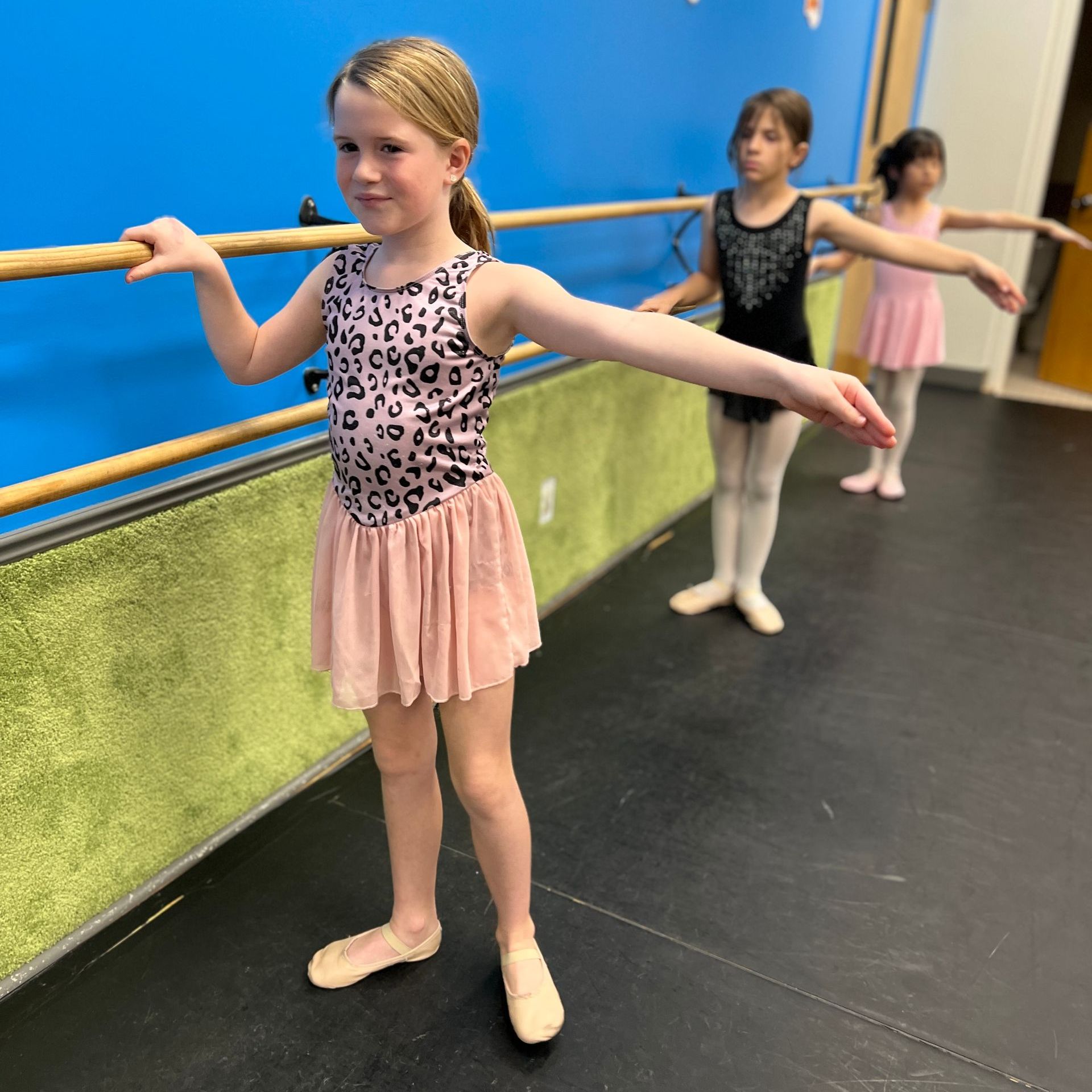 Three young girls are practicing ballet in a dance studio