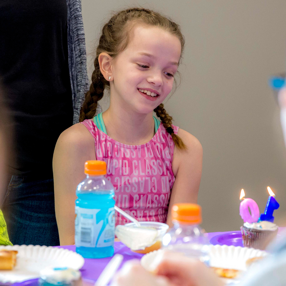A little girl is sitting at a table with a bottle of blue water celebrating her birthday