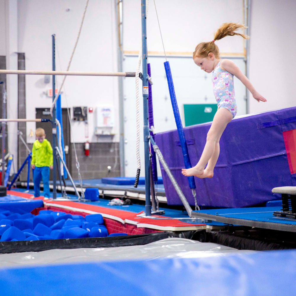 A young girl is jumping off a spring board into a pit a gym.