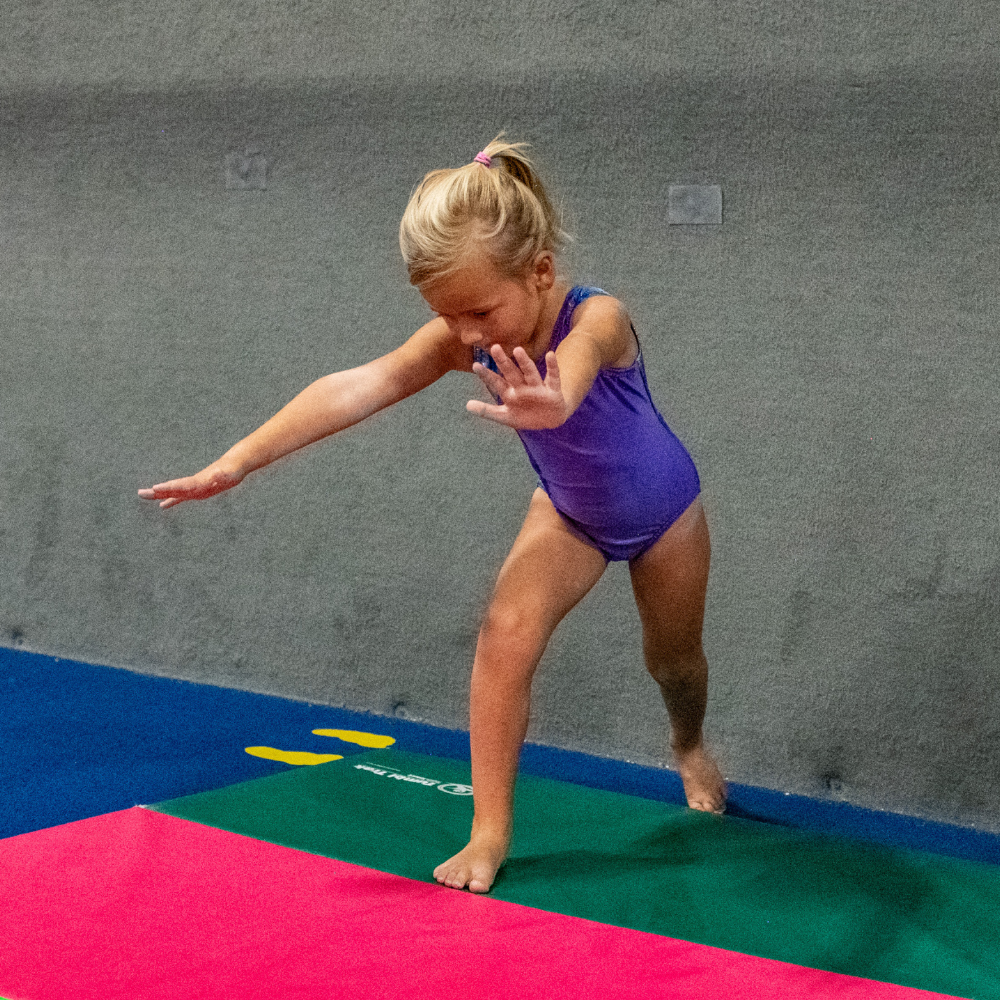 A little girl in a purple leotard is preparing for a cartwheel.