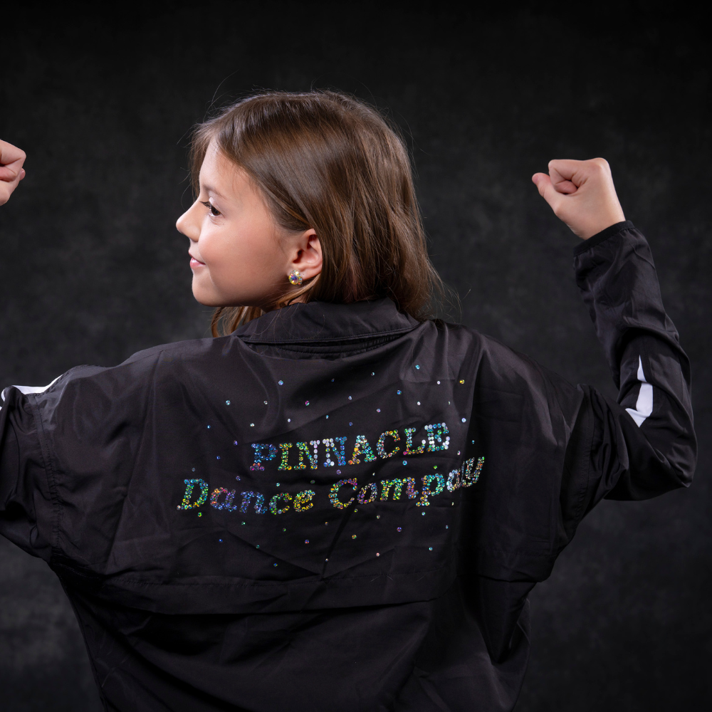 A young girl is wearing a pinnacle dance company jacket