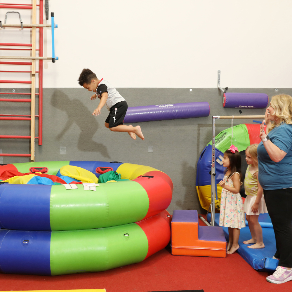 A boy is jumping in the air into a foam pit while a coach celebrates