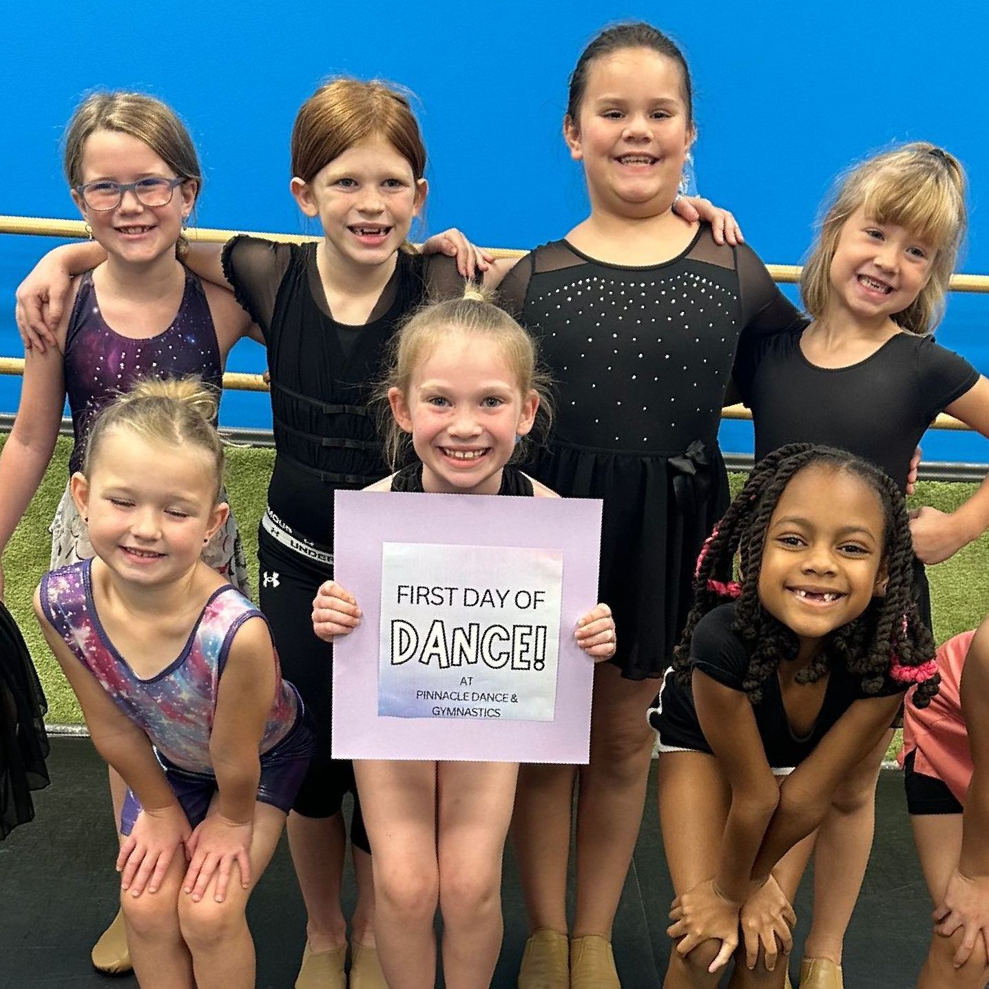 A group of young girls are posing for a picture and one girl is holding a sign that says first day of dance.