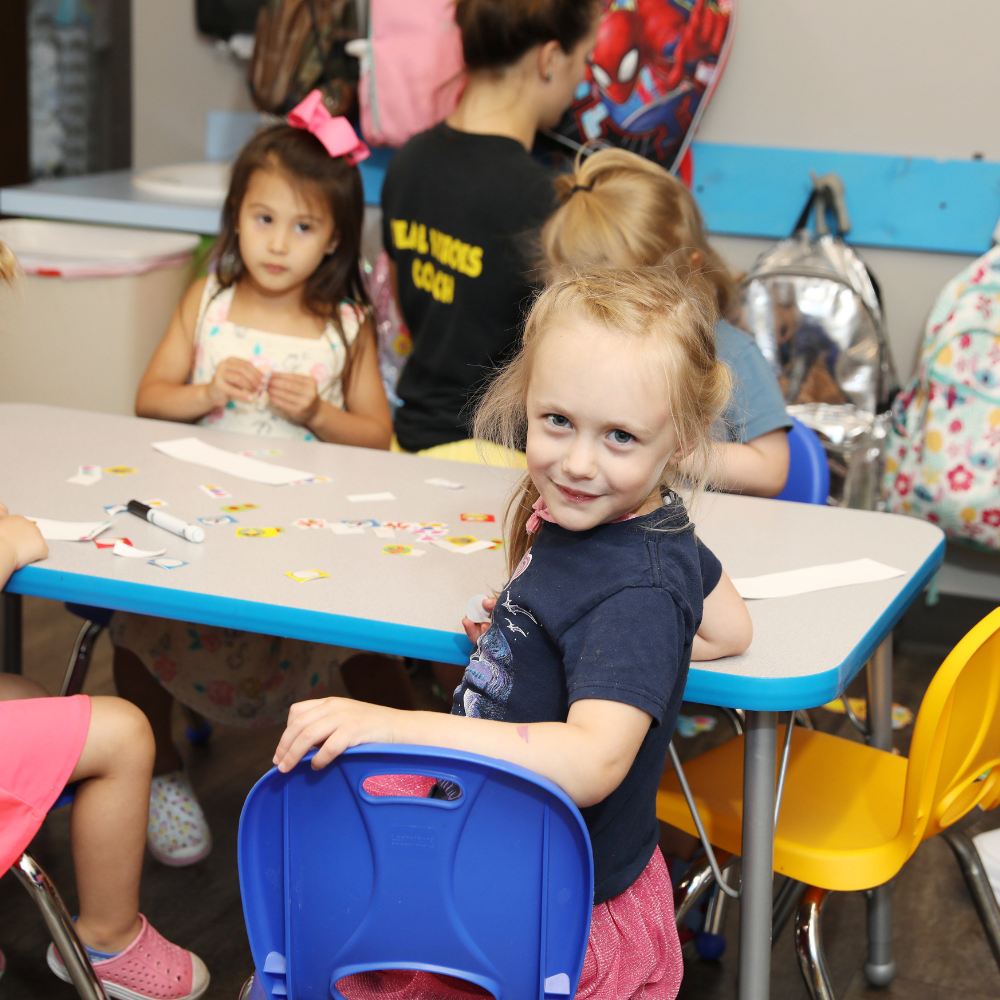 A girl wearing a black shirt that says ' spiderman ' on it is working on patterns at a table