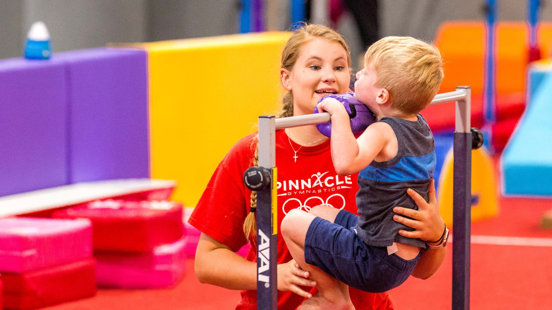 Four year old on a gymnastics bar doing a chin up with the help of a coach 