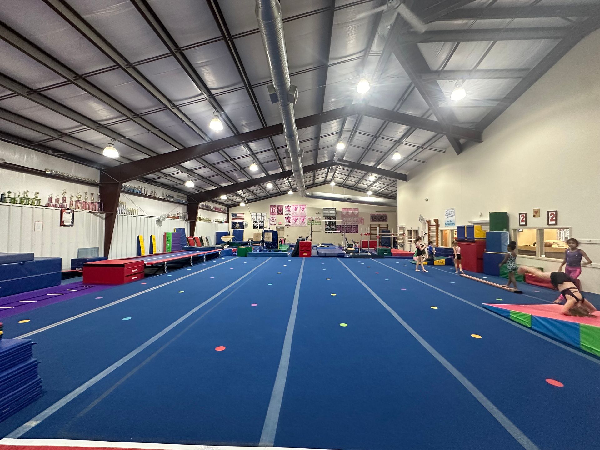 A large indoor Pinnacle Gymnastics with a blue mat and a lot of equipment.