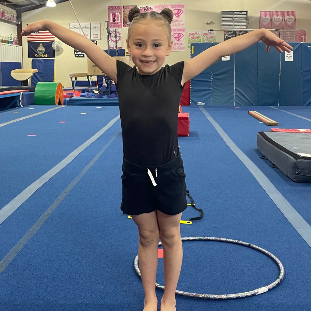 A little girl is standing in a gym with her arms outstretched