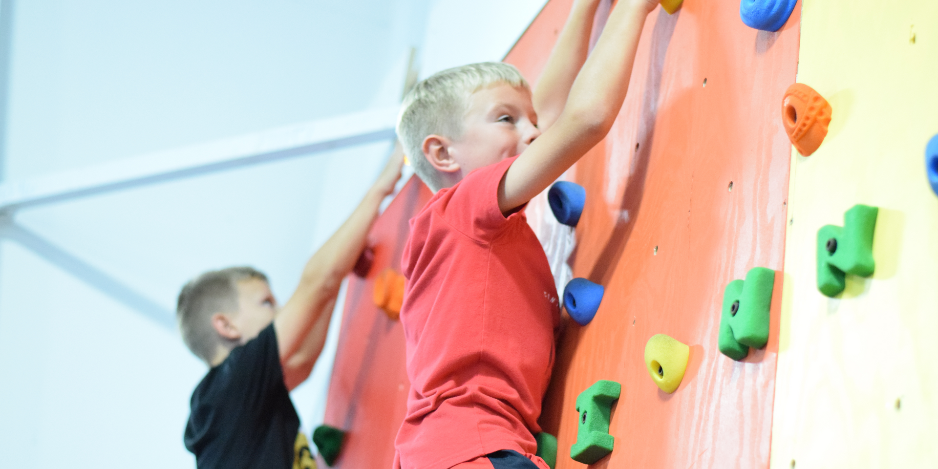 Boy in a red shirt climbing a rock wall with colorful hand grips.