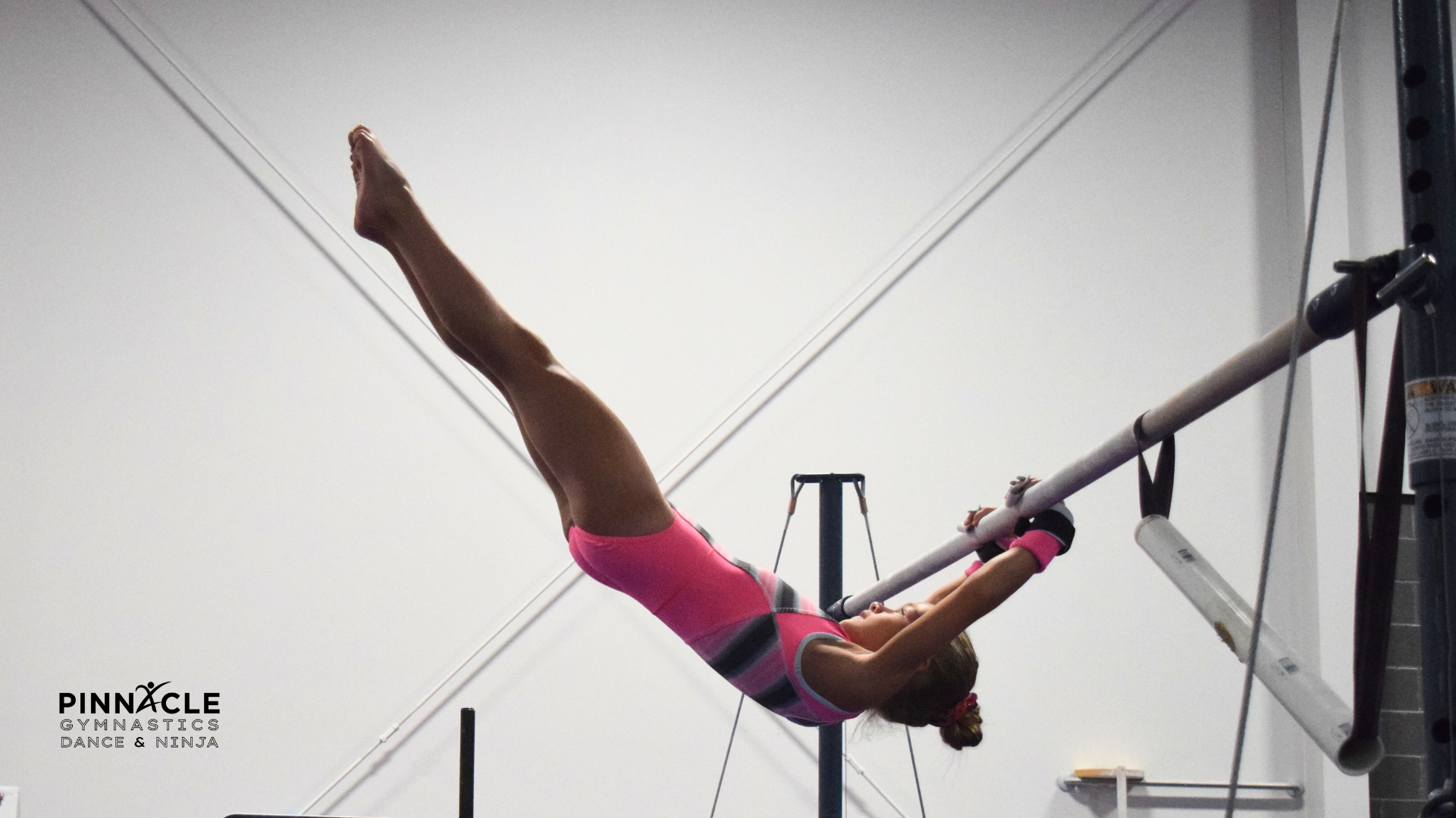 gymnast in a pink leotard performing a swing into a flyaway off the bar