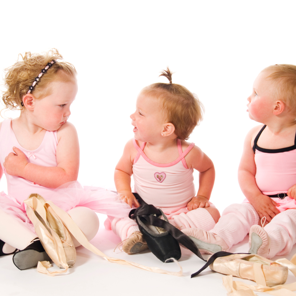 Three little girls are sitting on the floor with their ballet shoes