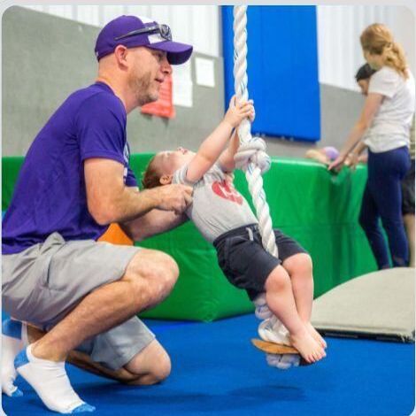 A dad helping his son swing on a rope.