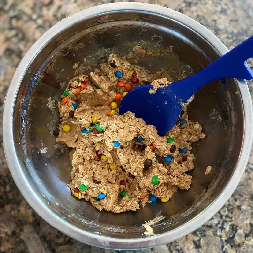 Protein ball ingredients being mixed together: includes oats, honey, peanut butter, protein powder, and M&Ms