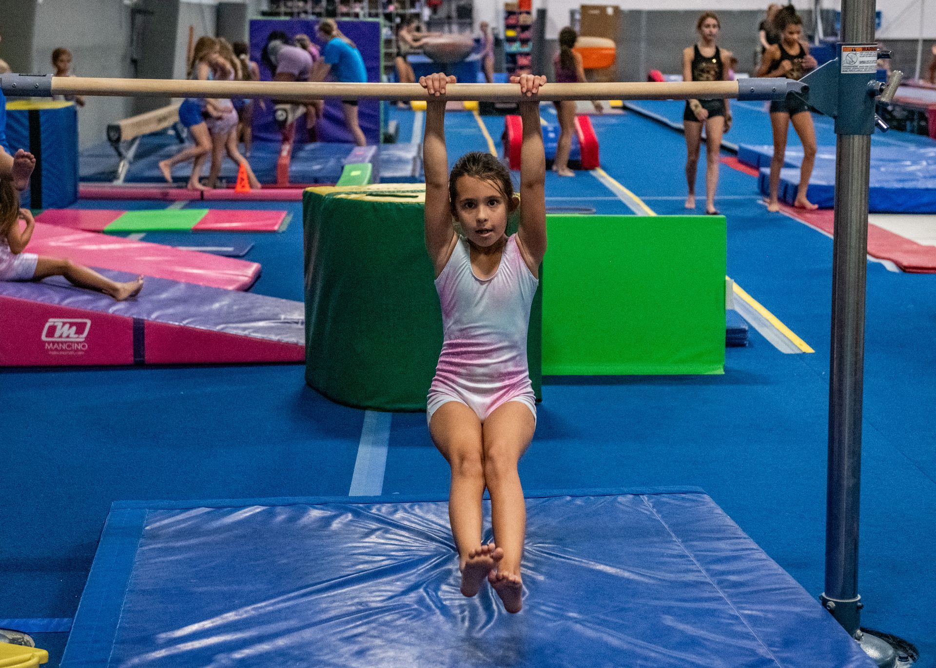 A young girl is doing a glide swing on a bar in a gym.