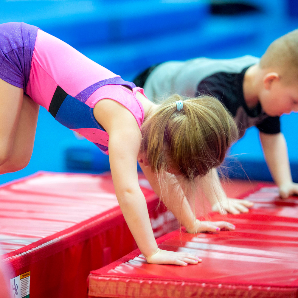 A boy and a girl are doing bear crawls on a red mat.