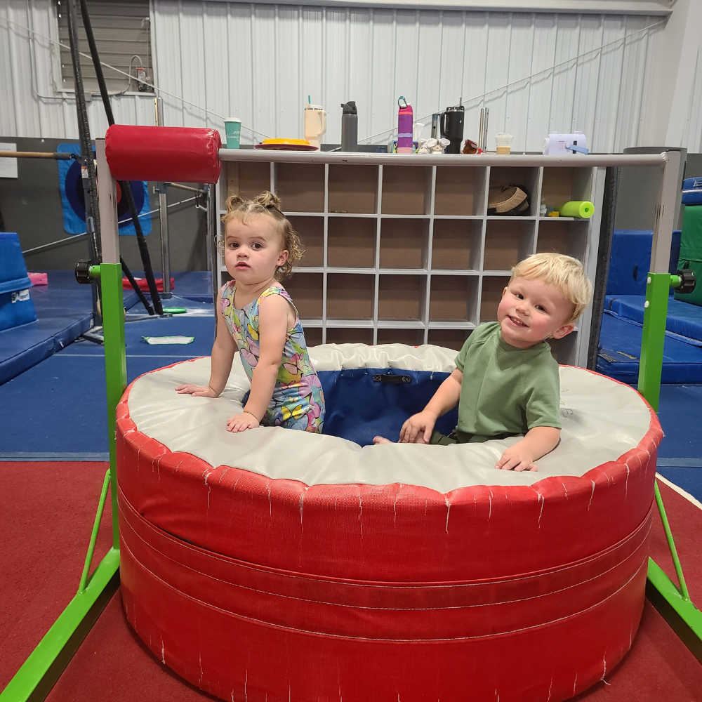 A boy and a girl are sitting in a donut mat in a gym.