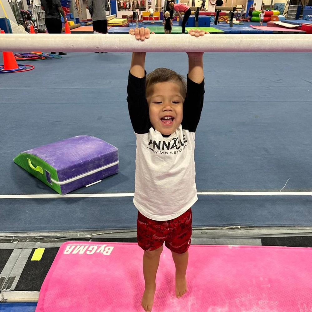 A boy hanging on a preschool gymnastics bar.