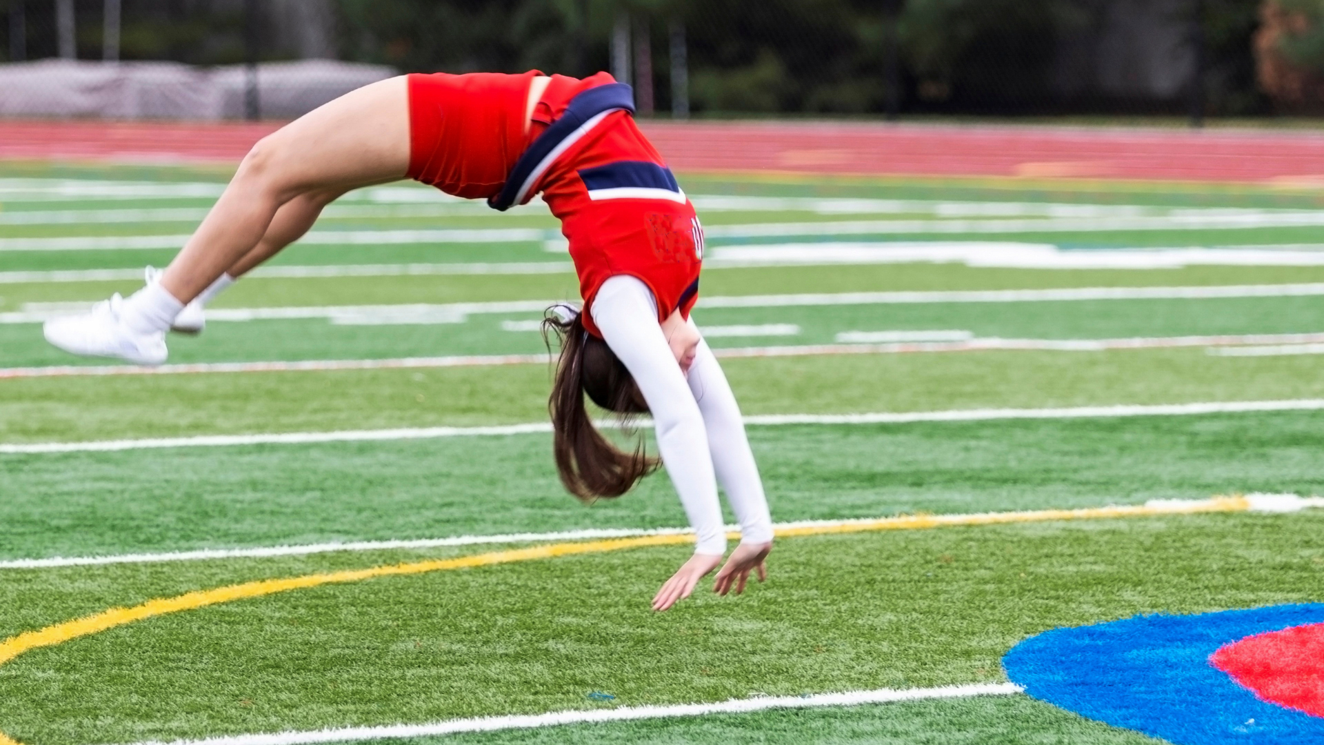 a girl in a red cheerleading outfit tumbling on a grass field doing a back handspring