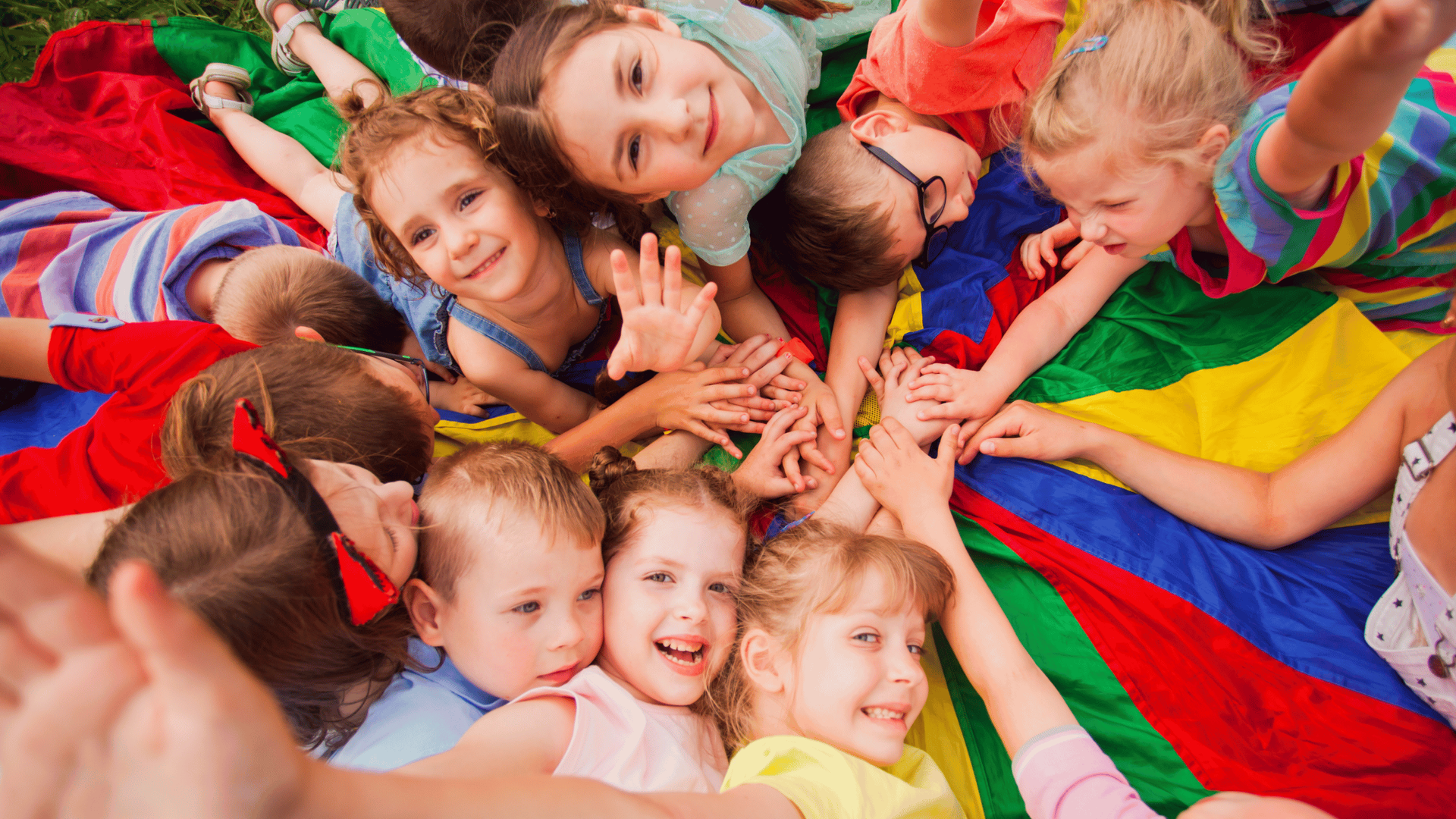 a group of kids cooperatively learning while using a parachute with colorful panels