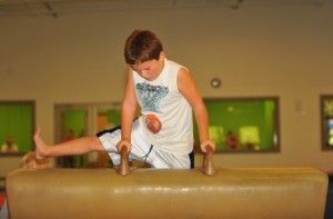 A young boy is doing the pommel horse at a gymnastics studio.